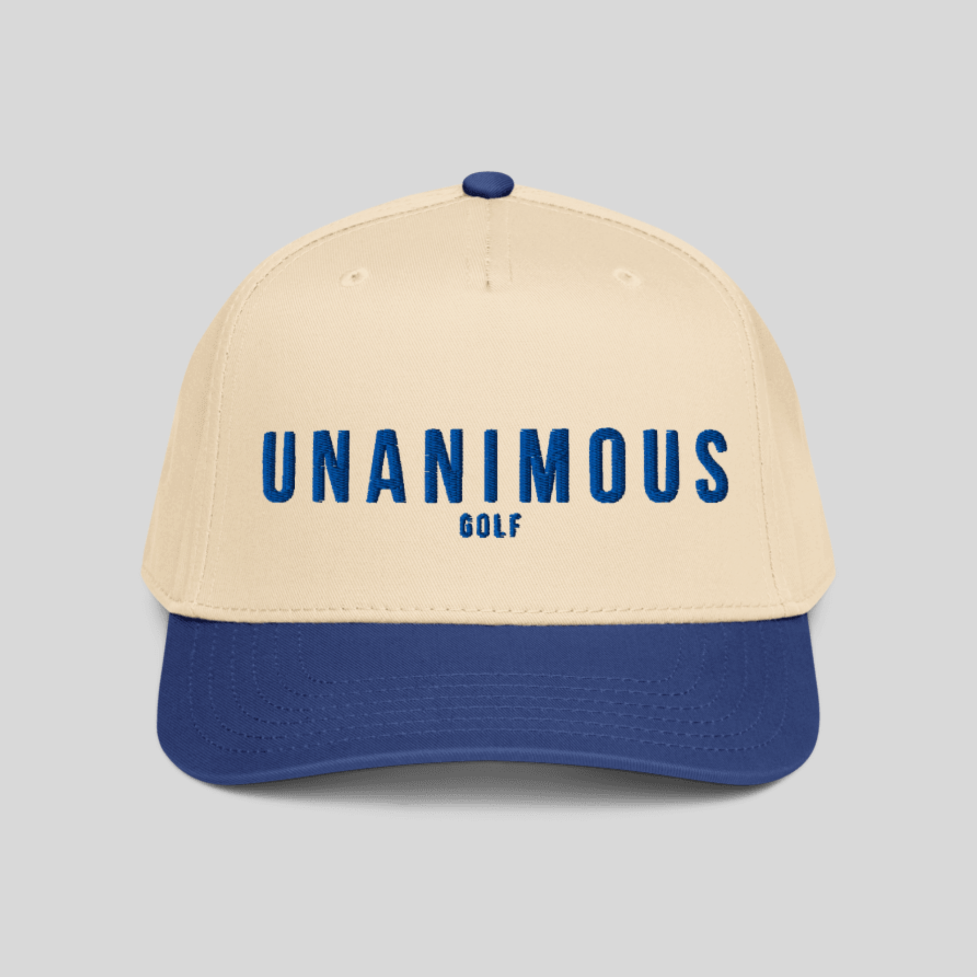 A structured baseball cap with a cream-colored crown and a royal blue visor, featuring the text 'UNANIMOUS GOLF' printed in blue on the front. The cap is photographed against a solid light gray background.