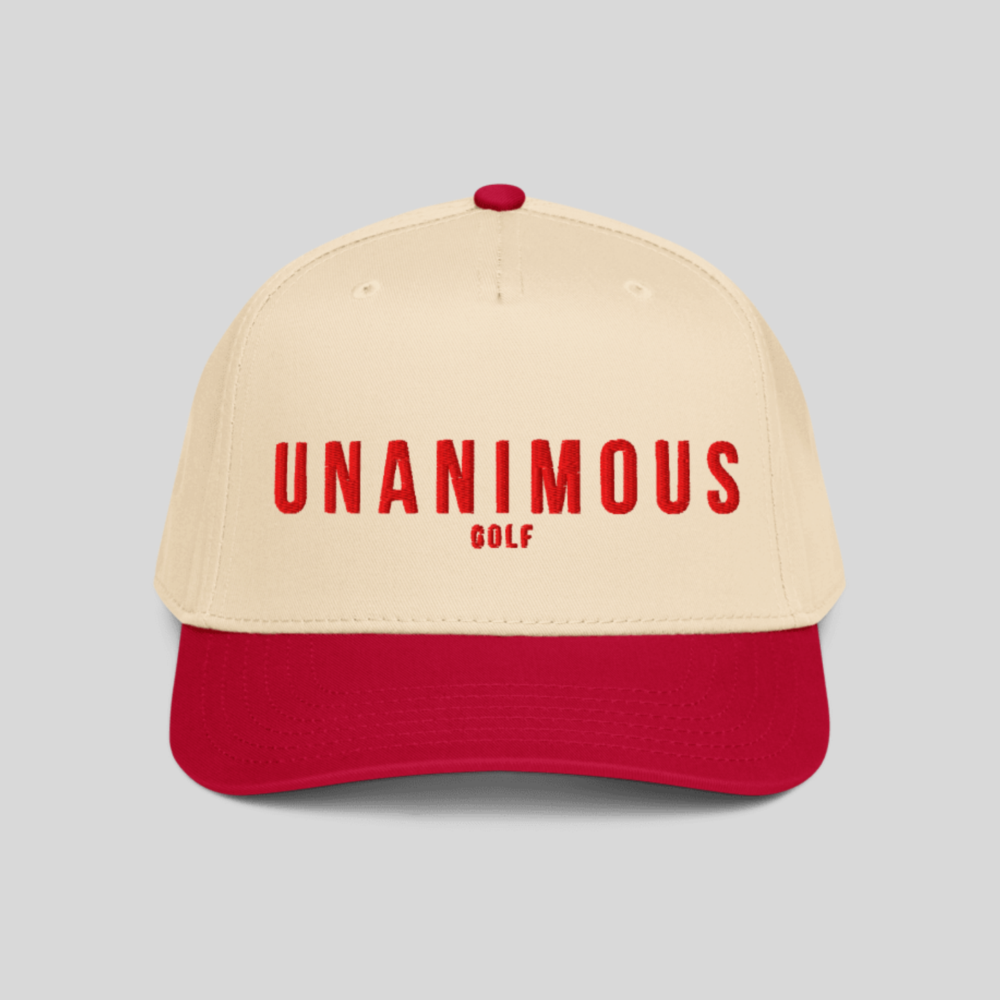 A two-tone baseball cap with a cream-colored crown and a red visor, featuring the text 'UNANIMOUS GOLF' in red on the front. The cap is shown against a solid light gray background.
