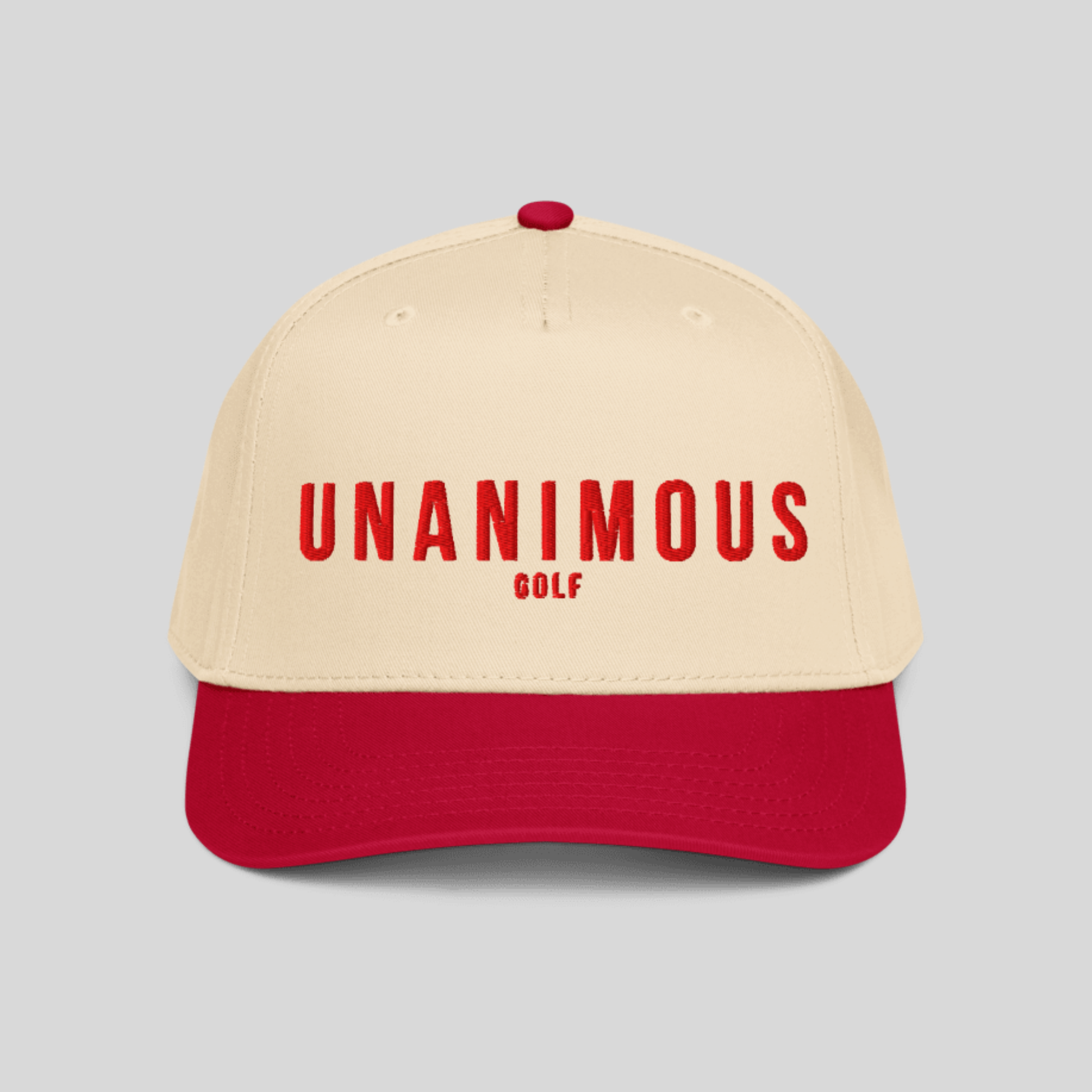 A two-tone baseball cap with a cream-colored crown and a red visor, featuring the text 'UNANIMOUS GOLF' in red on the front. The cap is shown against a solid light gray background.
